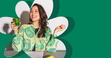 Vrouw op kantoor lacht terwijl ze snackgroente eet met een glas muntthee, als onderdeel van een gezond werkmoment.